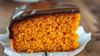 Fatia generosa de Bolo de Cenoura de Todo Dia, fofinho e alaranjado, com cobertura brilhante de chocolate escorrendo, em um prato branco.