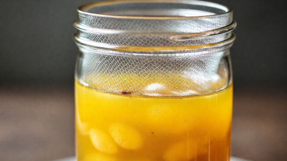 Close-up do caldo de peixe filtrado em jarra de vidro, destacando coloração clara e textura leve.