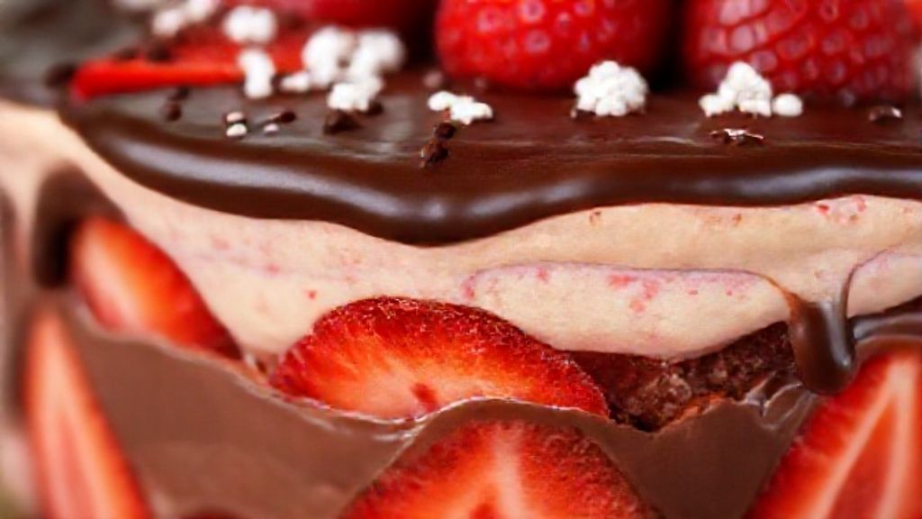 Close-up de uma fatia do pavê servida no prato, revelando camadas cremosas com morangos e cobertura de ganache