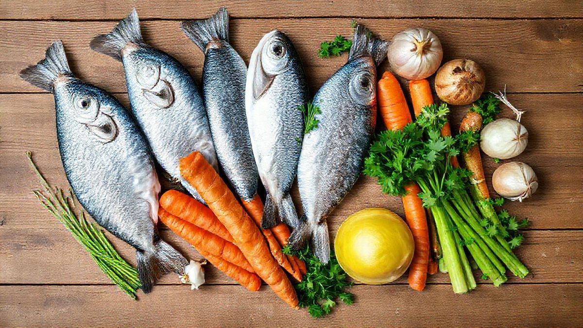 Vista de cima com cabeças de peixe, cebola, cenoura, salsão e ervas distribuídos em uma bancada rústica.