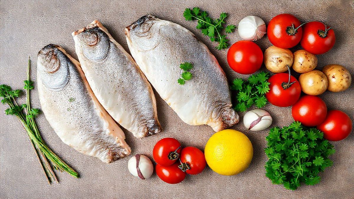 Visão de cima com postas de cação, batatas, cebola, tomate e temperos organizados em uma bancada.