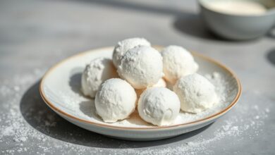Pequenos brigadeiros brancos e brilhantes dispostos em forminhas, com cobertura fina de leite Ninho e aparência suave e cremosa