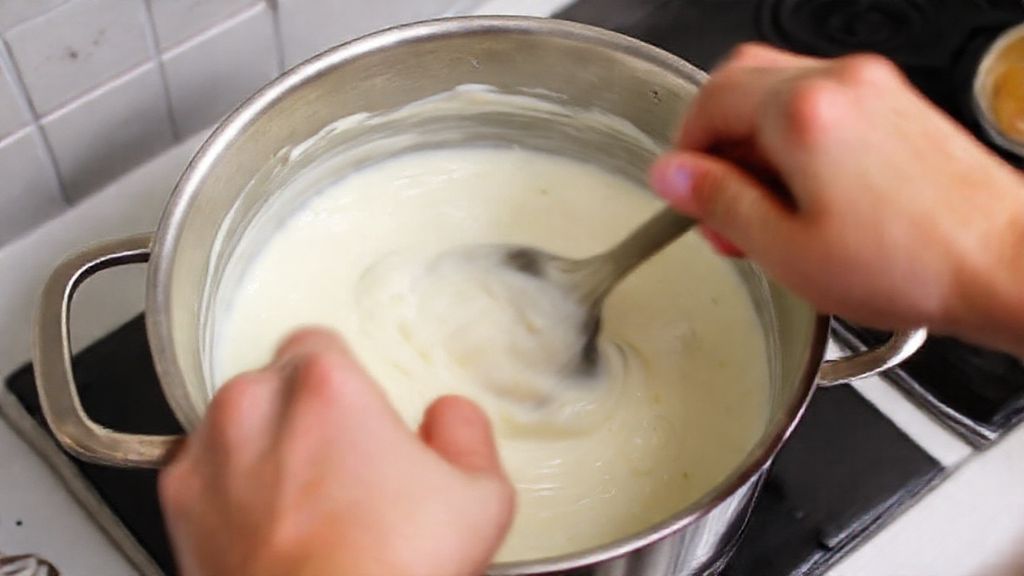 Mãos mexendo o creme branco em panela, mostrando o ponto cremoso ideal
