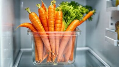 Cenouras vibrantes e frescas, algumas inteiras e outras em bastões, dispostas em um recipiente de vidro dentro da geladeira.