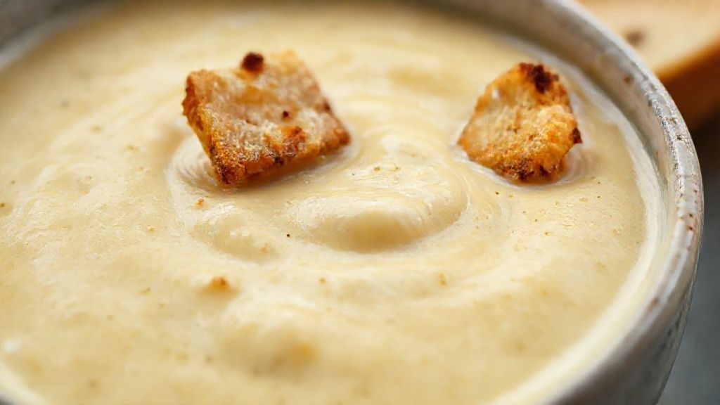 Close-up mostrando a textura aveludada da sopa cremosa com fio de azeite e croutons crocantes.