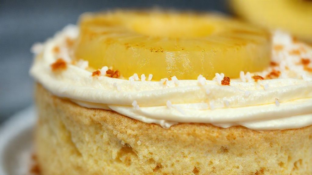 Close-up da torta gelada com textura cremosa, decorada com coco ralado e rodelas douradas de abacaxi