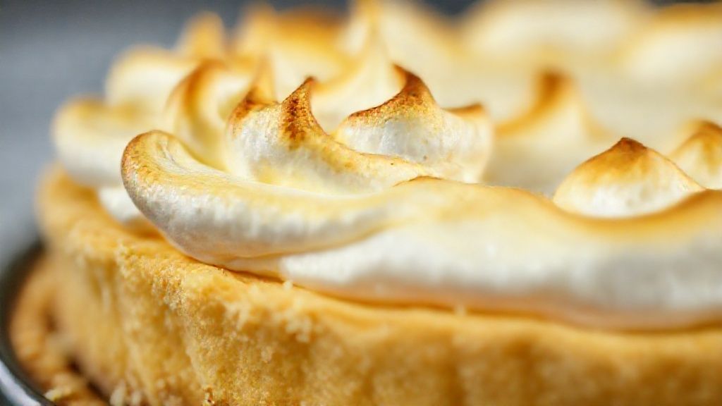 Close-up da torta cortada, mostrando as camadas de base, recheio cremoso e merengue dourado