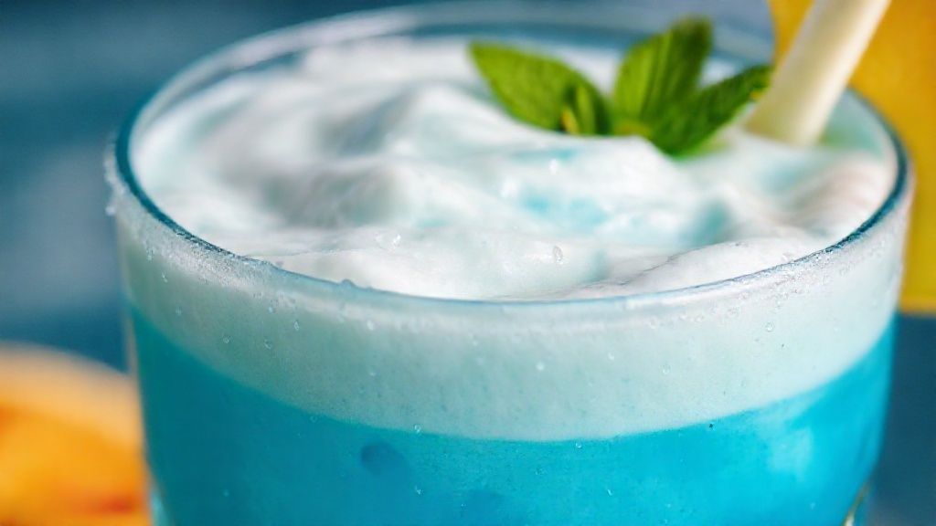 Close-up do coquetel azul com textura cremosa e brilho refrescante, decorado com frutas.