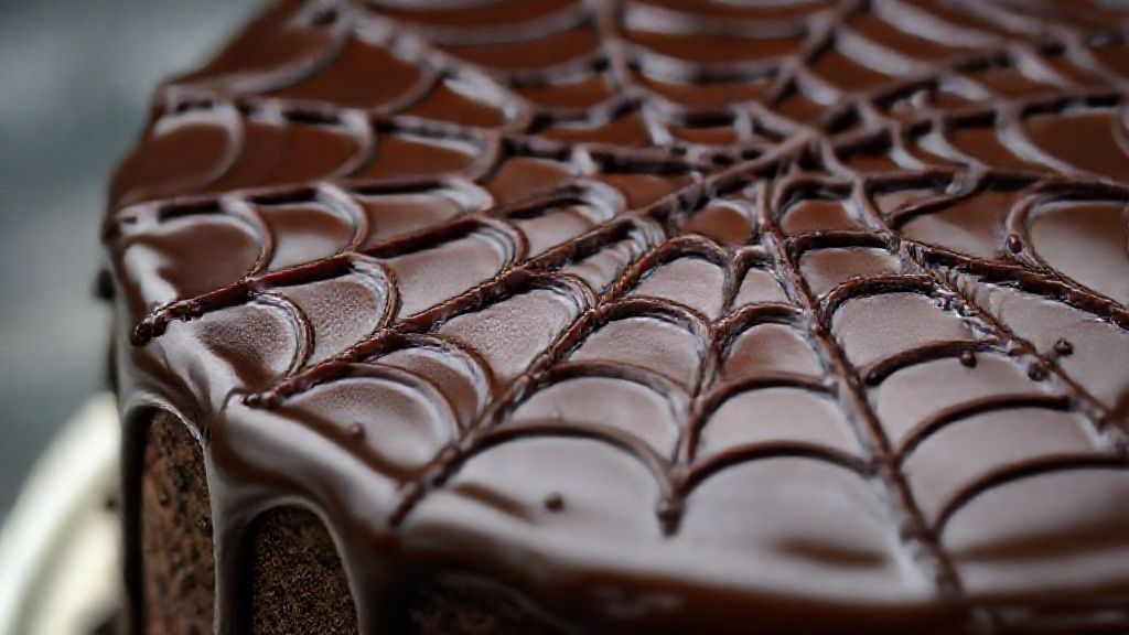 Close-up do bolo de chocolate com teia de aranha em destaque na cobertura.