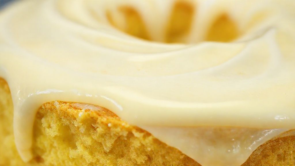Close-up mostrando a textura macia do bolo e o brilho da cobertura cremosa com raspas de limão