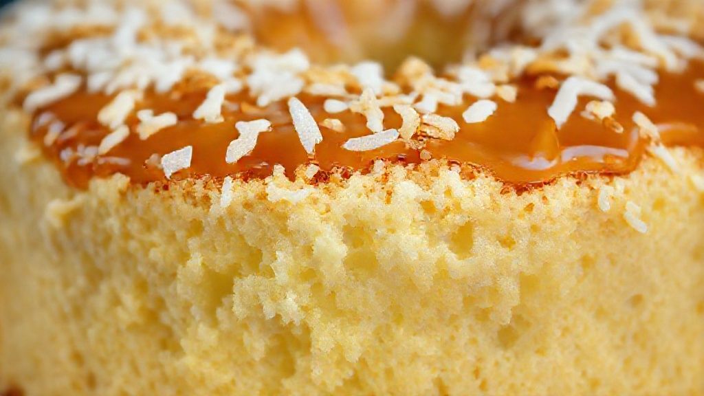 Close-up do bolo toalha felpuda mostrando textura molhadinha, coco ralado e brilho da calda.