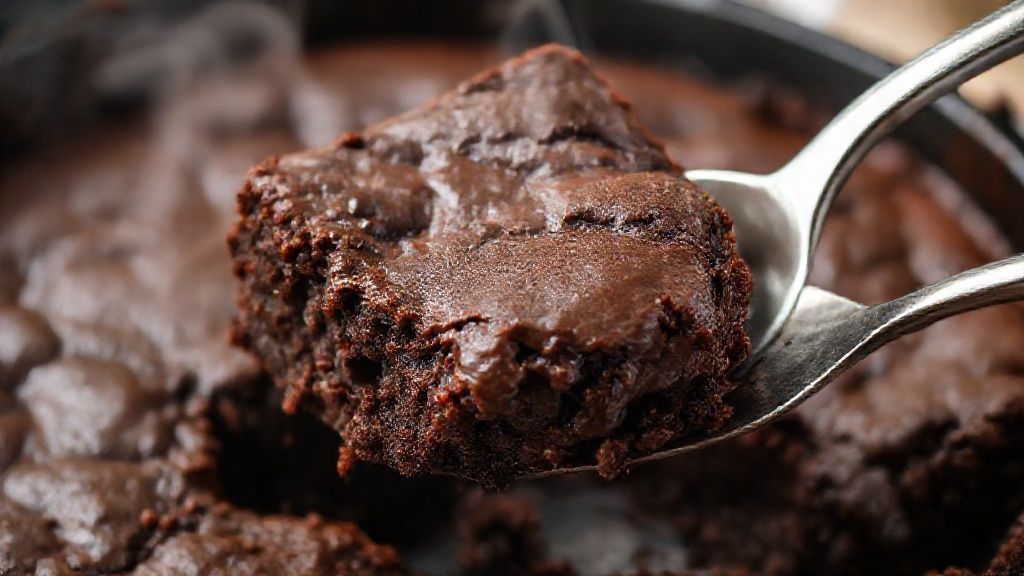 Close-up do brownie cremoso cortado na frigideira, mostrando o interior derretido.