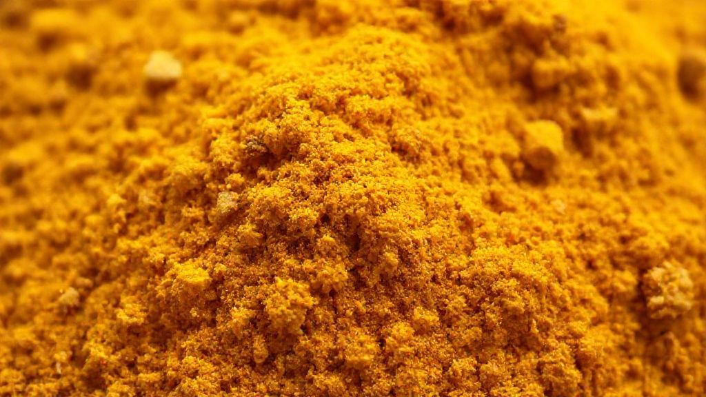 Close-up da textura do curry em pó pronto, destacando a riqueza de cores e granulação das especiarias.