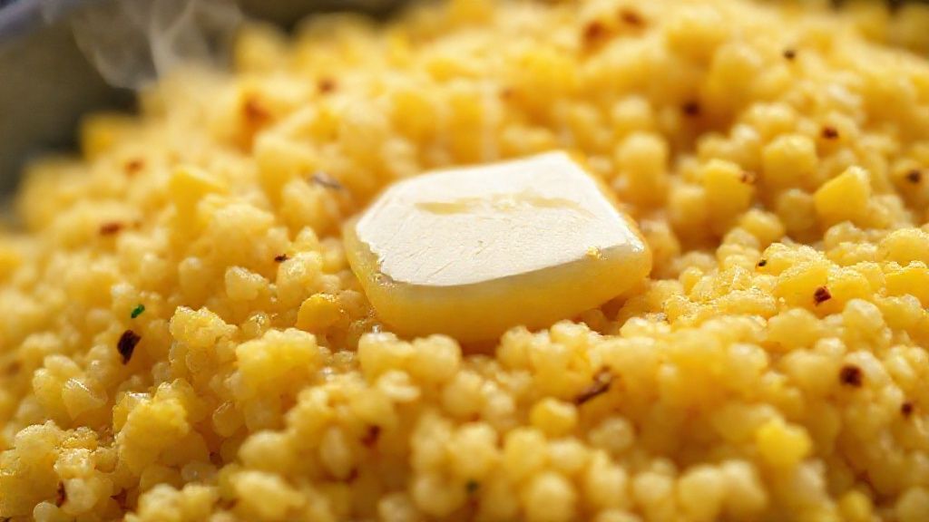 Close-up do cuscuz nordestino amarelinho mostrando textura soltinha e brilho da manteiga