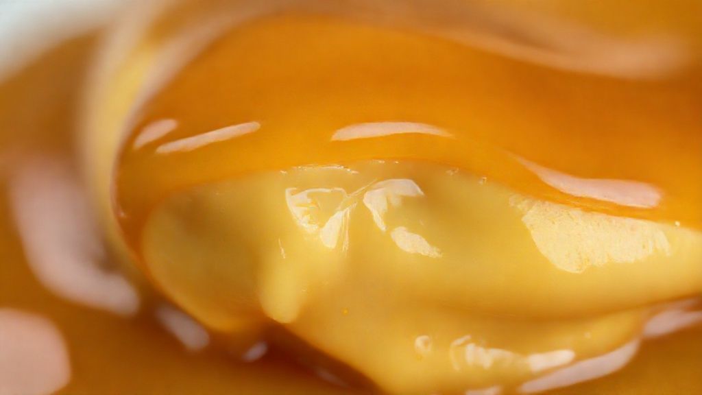 Close-up do doce de leite sendo retirado com colher, destacando a textura cremosa e o brilho