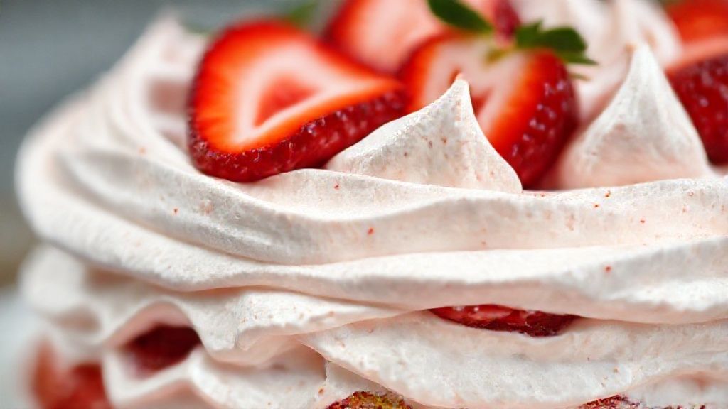 Close-up do doce mostrando as texturas do creme, merengue crocante e morangos frescos.