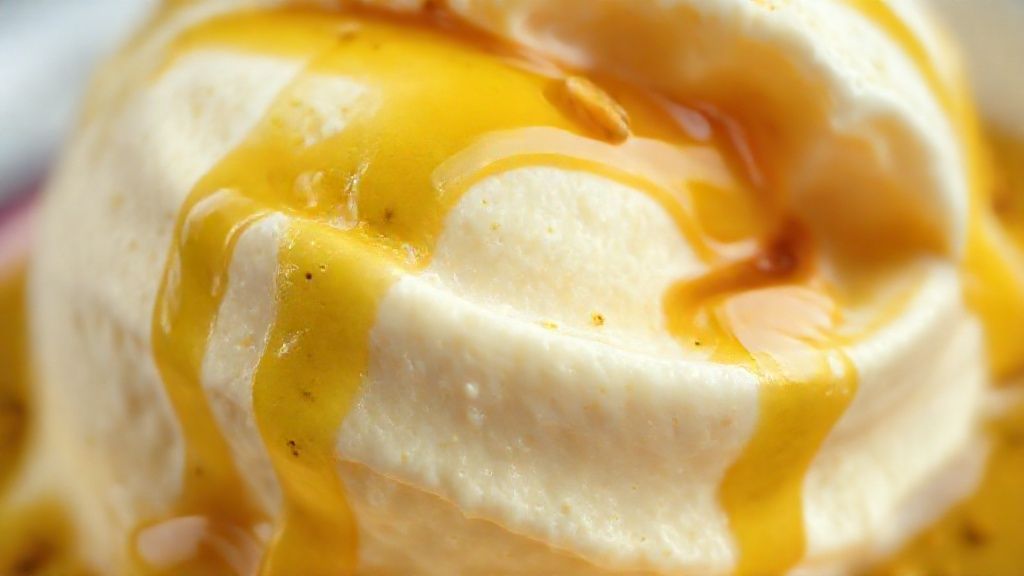 Close-up do sorvete mostrando textura aerada e a calda escorrendo sobre o topo com sementes de maracujá