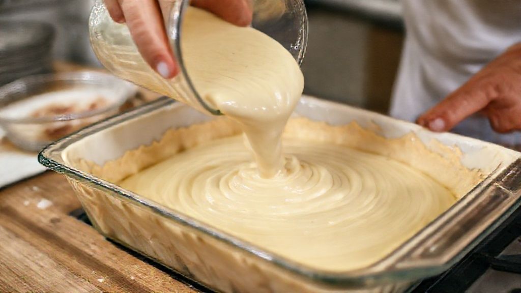 Mãos despejando a massa no refratário com o recheio cremoso de frango ao fundo.