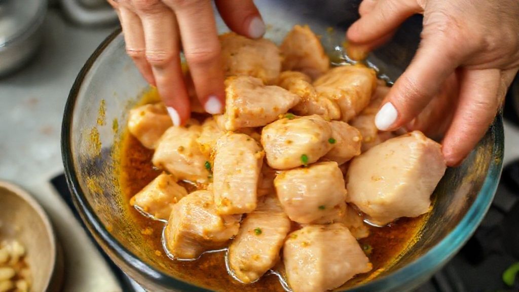 Mãos misturando o frango nos temperos em uma tigela, mostrando o processo da marinada