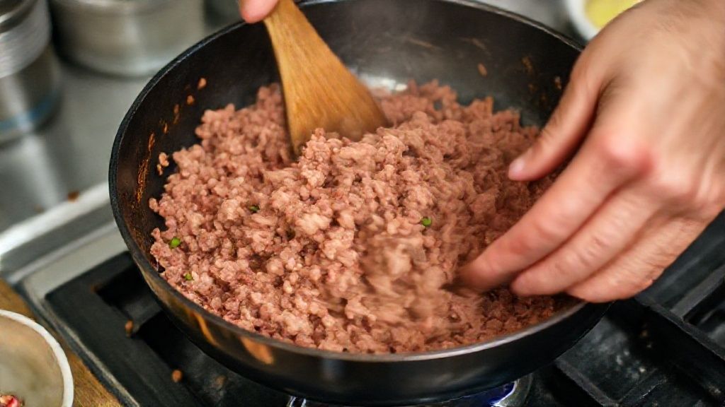 Mãos refogando carne moída e temperos em uma panela durante o preparo