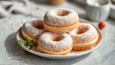 Rosquinhas douradas e fofas, cobertas com leite em pó e servidas em prato branco elegante.
