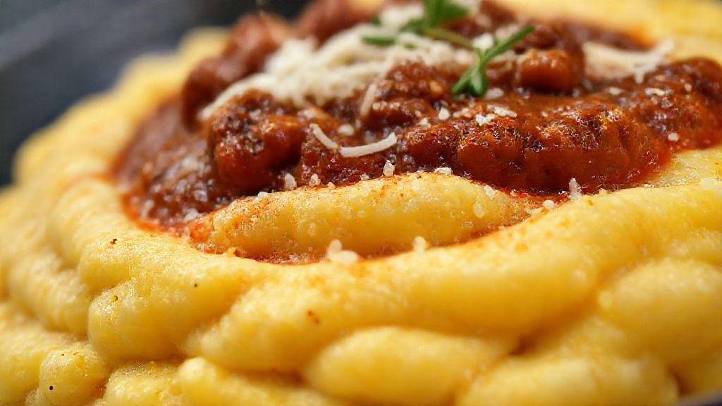 Close-up mostrando a textura da polenta cremosa com o ragu rico em molho