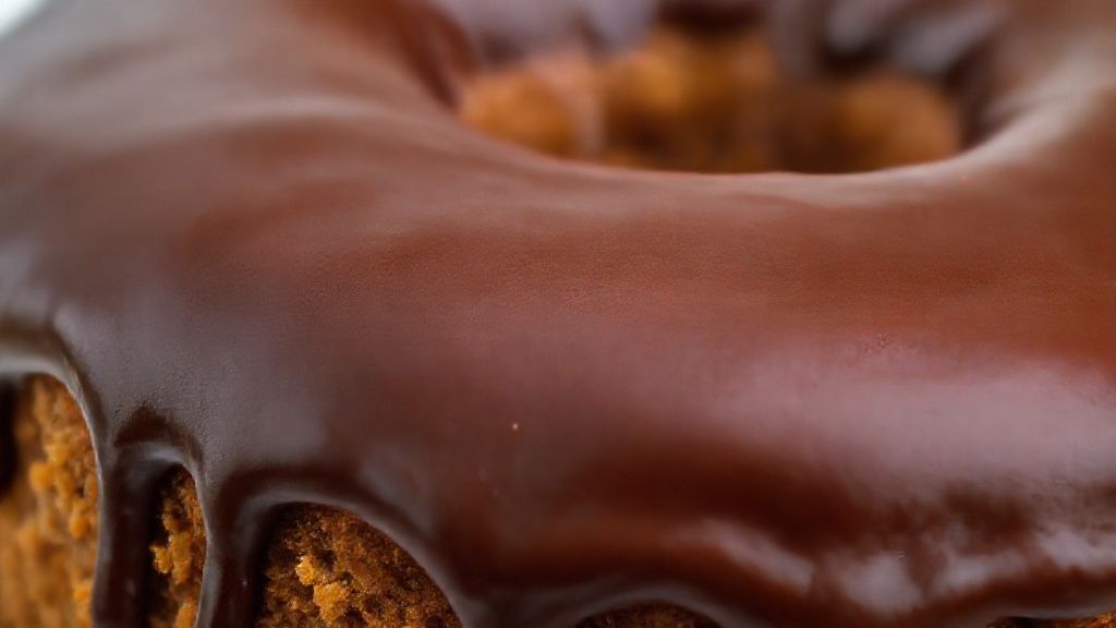 Close-up do bolo cortado revelando textura fofa e calda de chocolate brilhante escorrendo
