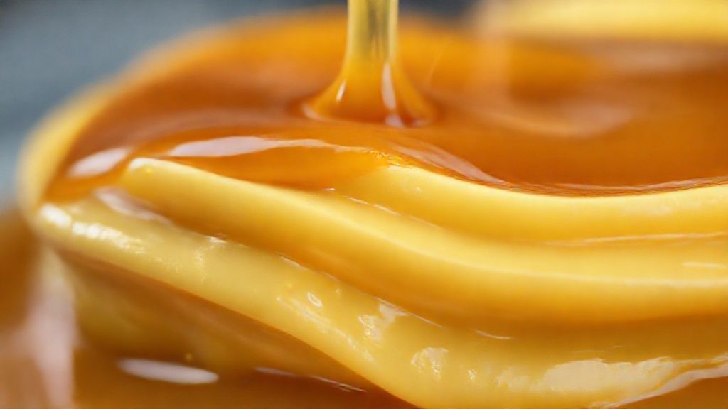 Close-up do doce de leite pronto, destacando brilho, textura cremosa e cor dourada