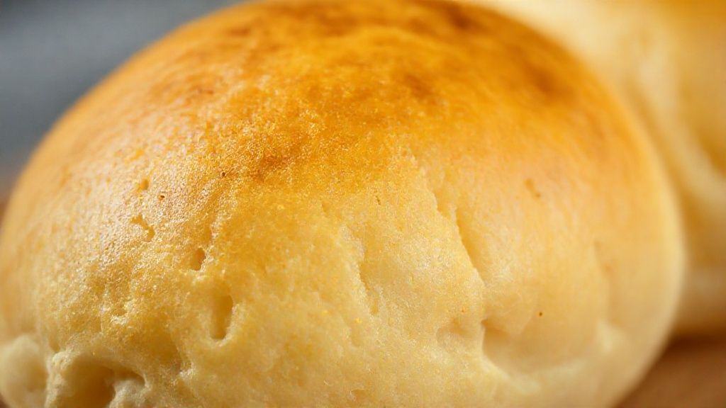 Close-up de um pãozinho de tapioca aberto mostrando o interior elástico e a casquinha dourada