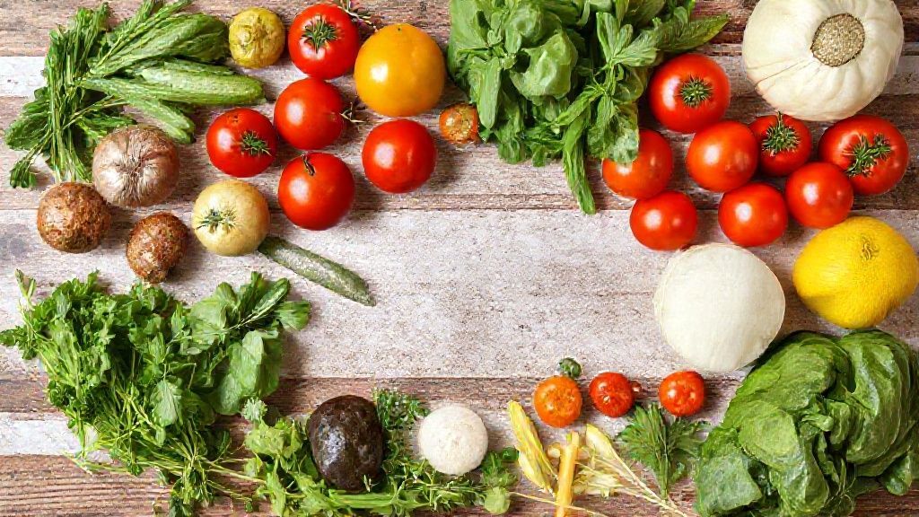 Ingredientes frescos dispostos sobre a bancada: abobrinhas, berinjelas, tomates, pimentões e ervas.