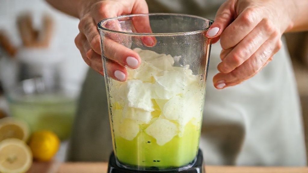 Mãos batendo a mistura verde de limão no liquidificador durante o preparo da receita