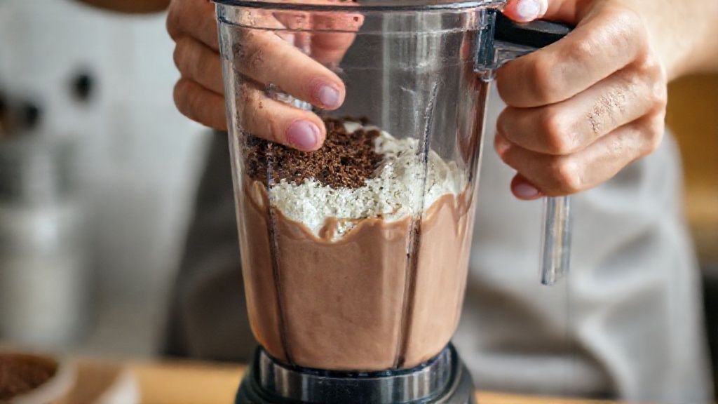 Mãos segurando o liquidificador enquanto mistura o sorvete e a calda de chocolate