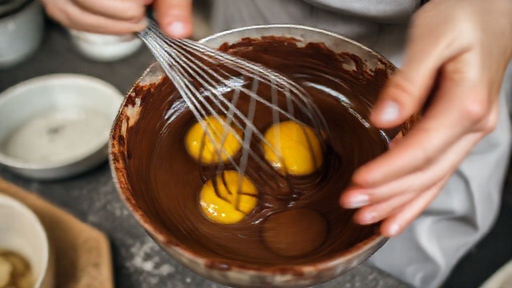 Mãos misturando chocolate derretido com ovos em tigela durante o preparo da torta