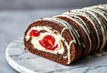 Rocambole de chocolate fatiado revelando recheio cremoso de leite em pó e geleia de morango
