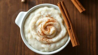 Tigela de louça branca com arroz doce cremoso, finalizado com canela em pó e um pau de canela ao lado.