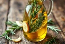 Frasco de vidro com azeite dourado e cristalino, infundido com ramos de alecrim verde e fatias de alho dourado.