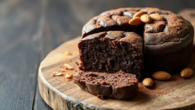 Bolo de chocolate denso e úmido, com crosta levemente craquelada e interior macio, fatiado sobre um prato de madeira rústico.
