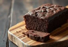Um bolo de chocolate escuro, fofinho e úmido, fatiado para revelar a textura macia, em uma superfície rústica de madeira.