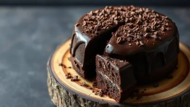 Um bolo de chocolate redondo, com cobertura de ganache brilhante e raspas de chocolate, fatiado para revelar o miúdo úmido e escuro.