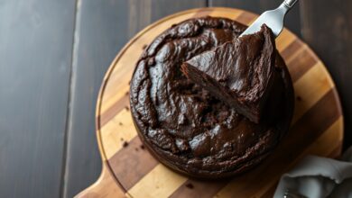 Um bolo de chocolate vegano redondo e denso, com uma fatia generosa sendo servida, revelando a textura úmida e fofa do interior.