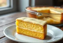Bolo de fubá cremoso em uma forma de vidro, com a superfície dourada e levemente ondulada, mostrando as duas camadas distintas ao ser cortado.