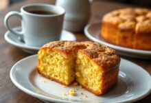 Bolo de fubá dourado com casquinha crocante no topo, fatiado revelando miolo macio e aerado, servido com café ao lado
