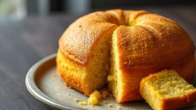 Bolo de fubá dourado e fofinho, fatiado, com textura úmida e visível, servido em um prato de cerâmica rústica.