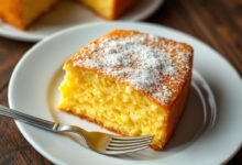Fatia generosa de bolo de milho com fubá, revelando a textura cremosa e granulada do interior amarelo-ouro contrastando com a fina casquinha dourada e ligeiramente rachada no topo.