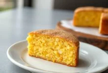 Bolo de milho dourado, com textura úmida e cremosa, fatiado para revelar o interior macio com grãos de milho.