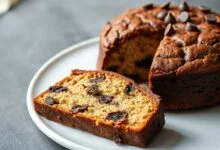 Um bolo dourado com pedaços de chocolate derretidos por cima, fatiado para revelar a textura macia e úmida.