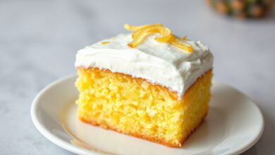 Fatia generosa de bolo gelado de abacaxi com creme firme e raspas de fruta, servido em prato branco.