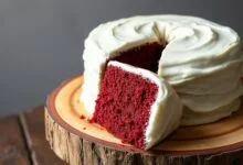 Um bolo red velvet natural de cor vermelho-escuro vibrante, coberto por uma camada generosa de glaceado cremoso e branco de cream cheese.