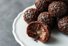 Brigadeiros perfeitos, escuros e brilhantes, enrolados em granulado, dispostos elegante em um prato branco.