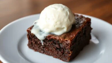 Fatia de brownie fudgy com casquinha crocante, centro úmido e denso, coberta por uma bola generosa de sorvete de baunilha derretendo lentamente, servida em um prato branco.